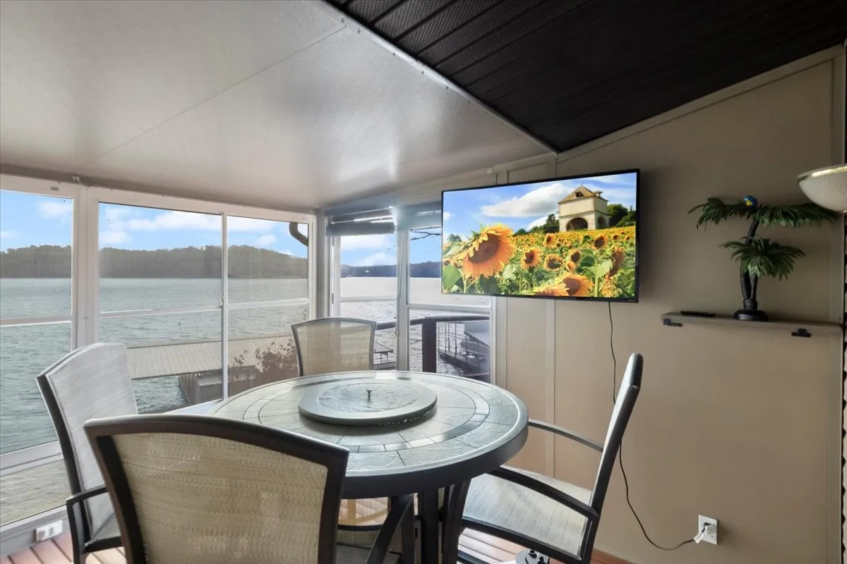 A tranquil and cheerful space featuring a round dining table, a sunflower-themed TV, and large windows overlooking water. The scene captures a group-friendly setting ideal for meals, conversation, and scenic enjoyment, reinforcing the sense of connection and comfort described in the section.