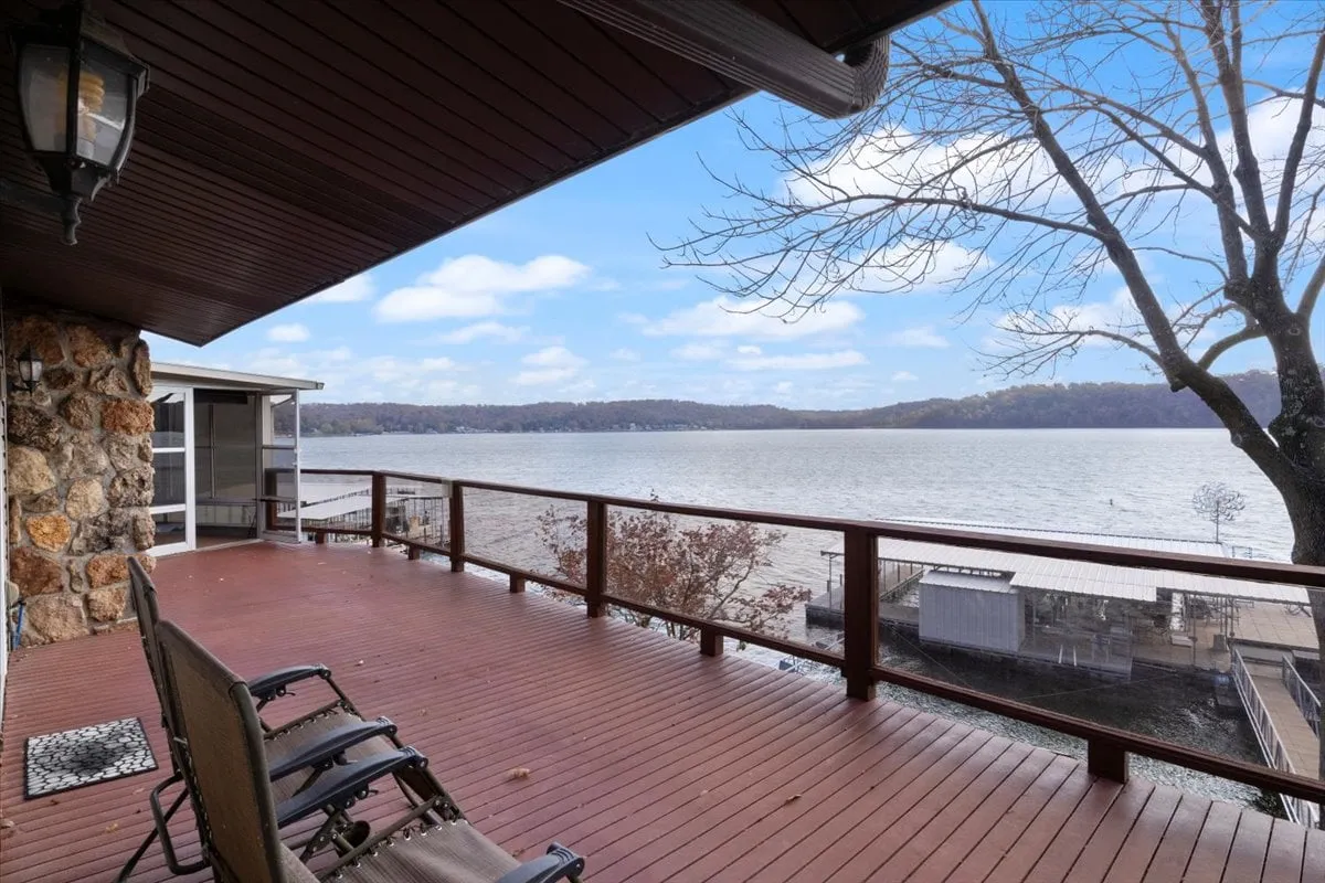 A wooden deck looking out over the lake with a backdrop of trees and a stone wall. The deck provides a peaceful setting for relaxation, gathering, and appreciating the natural beauty at different times of day.