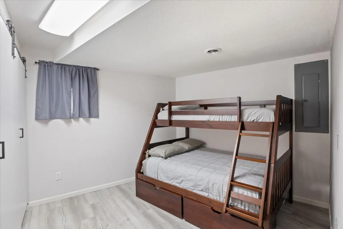 A cozy bedroom designed for children or groups, featuring a bunk bed, window with curtain, and built-in storage drawers beneath the bed. The inviting layout supports both rest and play, enhancing family experiences.