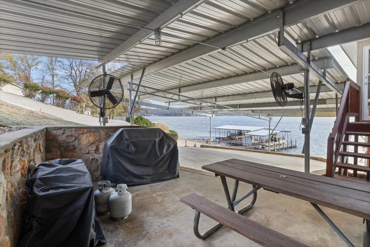 A covered outdoor seating area equipped with a barbecue grill faces the lake. The space is designed for casual meals, socializing, and enjoying the natural surroundings in comfort, blending indoor amenities with an outdoor experience.