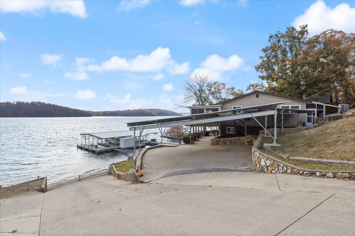 A peaceful shot of the waterfront with a boat dock, beautifully landscaped garden, and carport in view. The scene captures the serenity of lakeside living, with the dock providing direct access to fishing, boating, and other water activities.