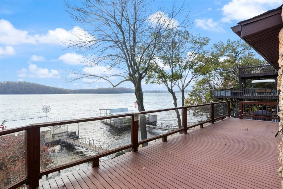 An expansive wooden deck extends toward the lake, framed by lush trees and a breathtaking view across the water. The deck is spacious enough for gatherings, outdoor dining, or sunset watching, embodying the freedom and open-air lifestyle highlighted in the section. The morning light and tranquil surroundings enhance the sense of lakeside escape.