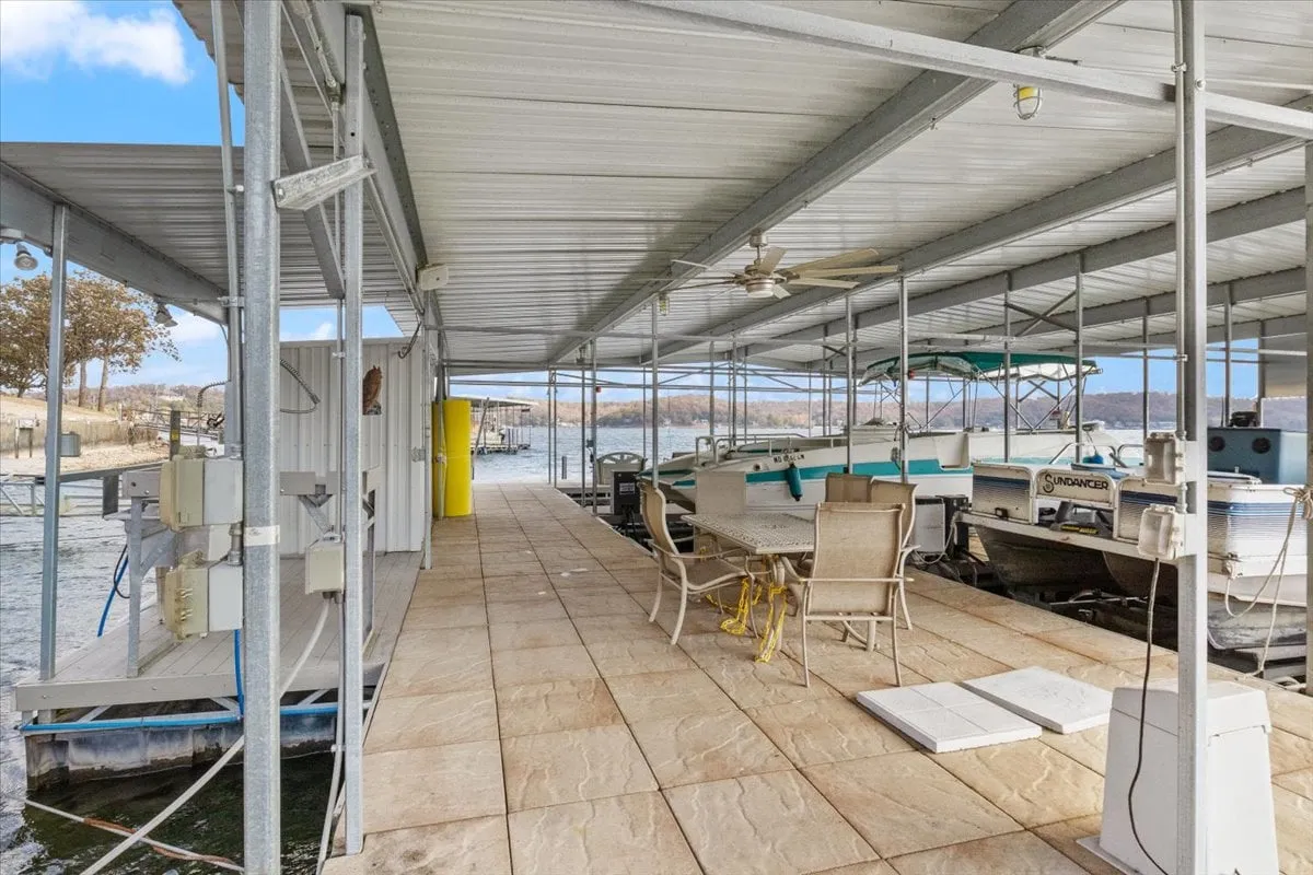 A lively dockside scene with boats docked along the water, ample seating for relaxing, and a yellow storage unit, suggesting areas for fish cleaning or watersports gear. The setting is casual and perfect for gatherings.