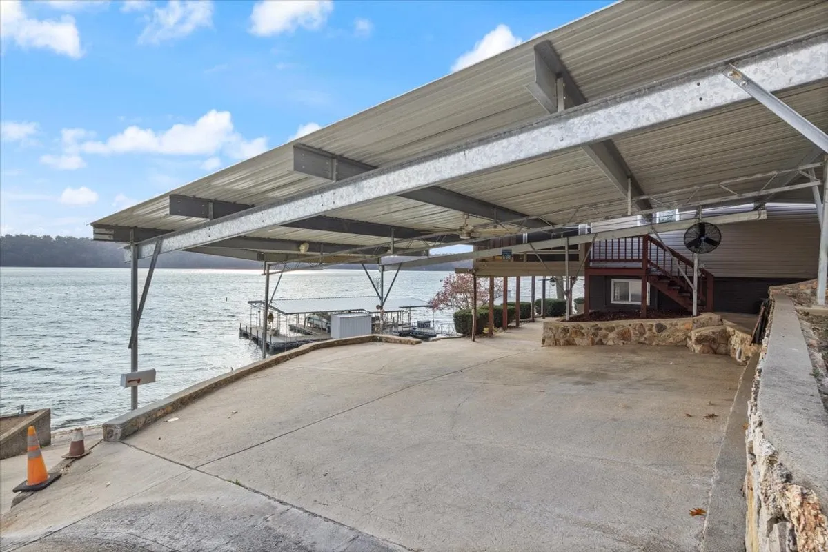This image features a covered parking area adjacent to the waterfront, with a visible staircase leading up to the house. The lakefront view in the background ties the property to its scenic context, while the generous parking area directly supports the section’s emphasis on convenience and accessibility for guests arriving by car.